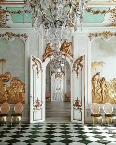 an ornate hallway with chandelier, chairs and paintings on the wall behind it