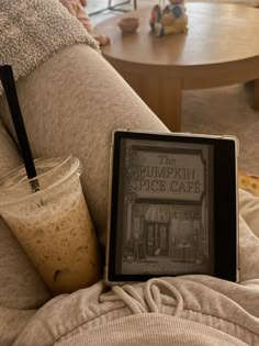 a coffee cup sitting on the arm of a couch next to a book titled pumpkin spice cafe