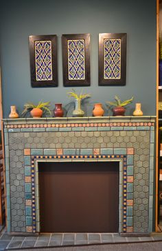 a fireplace in a living room with two paintings on the wall and vases on top