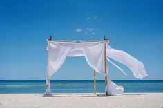 an outdoor wedding setup on the beach with white draping and blue water in the background