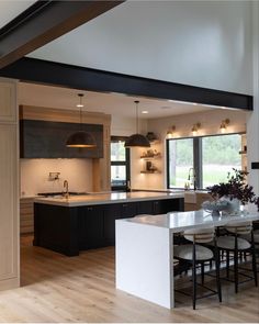 a large open kitchen and dining room area with wood flooring, white counter tops and black cabinets