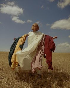 a woman in a field with her arms out and two dresses draped over her shoulders