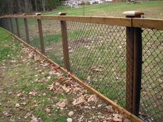 a wooden fence is next to a grassy field with leaves on the ground and houses in the background