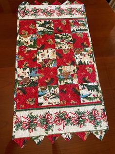 a quilted table runner with red and green flowers on it sitting on a wooden surface