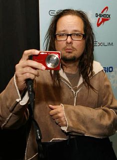 a man with long hair and glasses holding up a red camera