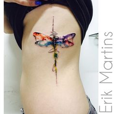 a woman's stomach with a colorful dragonfly tattoo on her side ribcage