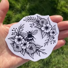 a hand holding a sticker with flowers and a bee on it's side