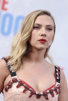 a woman with very large breast standing in front of a white wall and wearing a pink dress