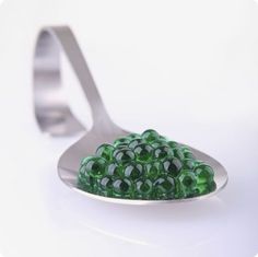 a spoon filled with green beads sitting on top of a white table next to a fork