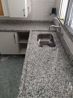 a kitchen counter top with a sink and window in the backround, next to cabinets