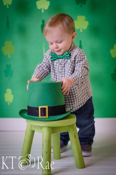 a baby boy in a green hat and bow tie playing with a small wooden stool