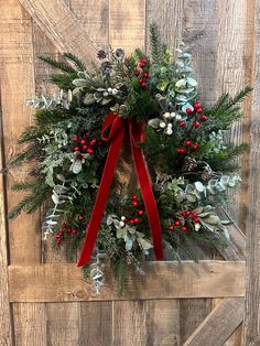 a christmas wreath hanging on the side of a wooden door with red ribbon and evergreens