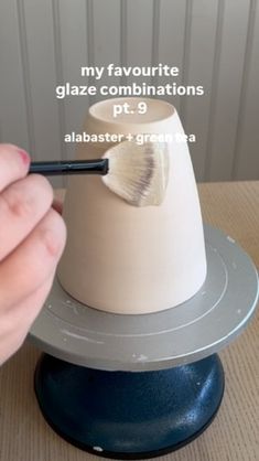 a person holding a brush in their hand near a white and gray cup on top of a table