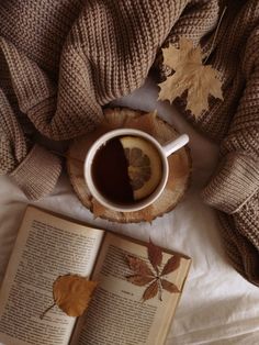 an open book, cup of coffee and maple leaves on a bed with white sheets