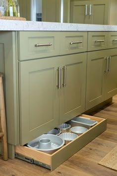 an open drawer in the middle of a kitchen with plates and bowls on it's bottom shelf