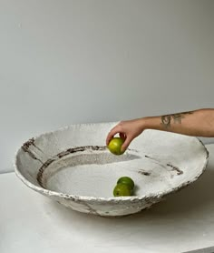 a hand reaching for an apple in a bowl on top of a white countertop