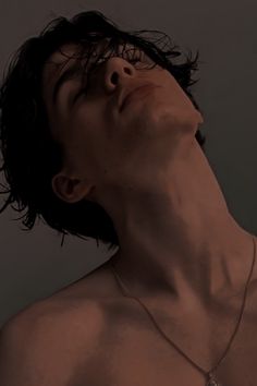 a man with no shirt on wearing a necklace and looking up at the sky in front of him