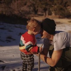 a man kneeling down next to a little boy in the snow holding a shovel and looking at him