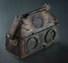 an old, rusty box with metal handles and knobs on the front is sitting on a black surface