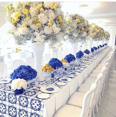 a long table with blue and white flowers in vases on the top, surrounded by chairs