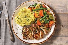 a white plate topped with meat and veggies next to mashed potatoes on top of a wooden table