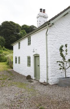 a white building with a green door and window next to a gravel road in front of it