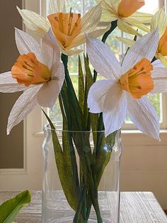 a vase filled with white and yellow flowers on top of a table next to a window