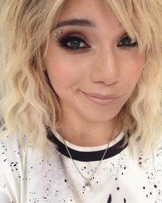 a close up of a person with blonde hair and black eyeliners smiling at the camera