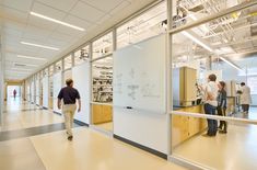 two men walking down a hallway in an office building with whiteboards on the wall