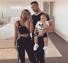 a man and woman holding a baby taking a selfie in front of a bed