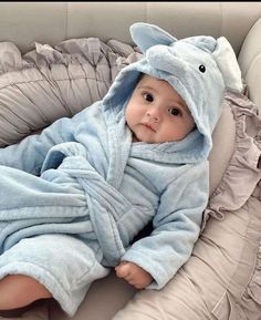 a baby in a blue elephant robe laying on top of a couch wearing a blanket