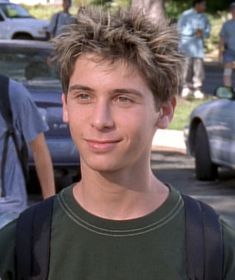 a young man is standing in front of parked cars and looking at the camera with a smile on his face