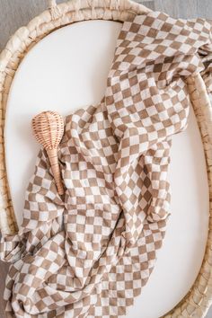 a wicker basket with a brown and white checkered cloth on it next to a wooden spoon