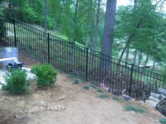 a fenced in area next to trees and rocks with a trash can on the ground