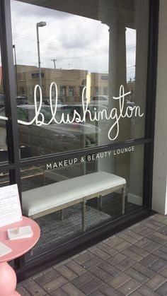 the front window of a makeup and beauty lounge with a bench in front of it