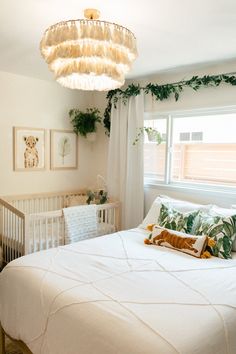 a white crib in a room with plants on the wall and a chandelier hanging from the ceiling