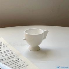 a white cup sitting on top of a table next to a piece of paper