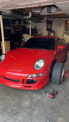 a red sports car parked in a garage next to a pile of tools and equipment