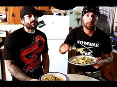 two men standing in a kitchen holding plates of food