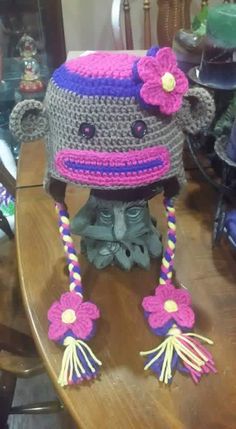 a crocheted monkey hat with flowers on it's head sitting on top of a wooden table