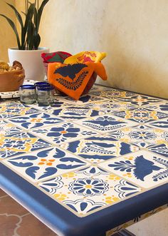 a blue and yellow patterned table cloth on top of a wooden table with potted plants in the background