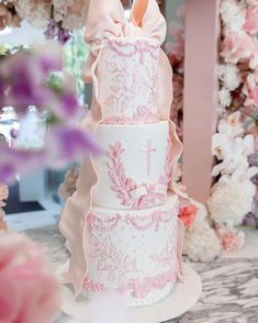 a three tiered cake decorated with pink flowers and a cross on the top layer