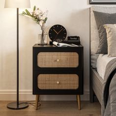 a nightstand with a clock on it next to a night stand and a flower vase