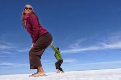 two people standing in the snow playing with a frisbee on a sunny day