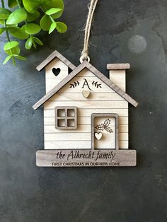 a wooden house ornament hanging from a string on a black surface with a plant in the background