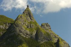 the top of a mountain with a bird perched on it's head and clouds in the background