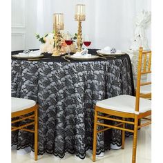 a black table cloth with white flowers and gold candles on it is set up for a formal dinner