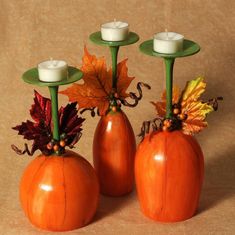 three pumpkin shaped candlesticks with leaves on them and one candle holder in the middle