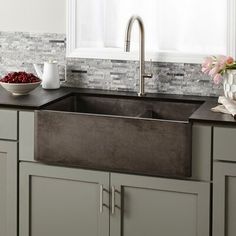 a kitchen sink sitting under a window next to a bowl of fruit and coffee pot