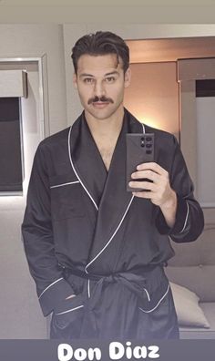 a man taking a selfie with his cell phone while wearing a black bathrobe